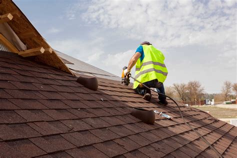 Construction Worker Putting The Asphalt Roofing Shingles With Nail