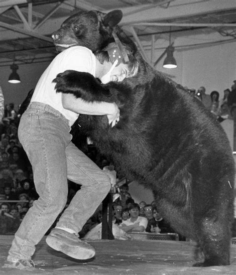A Man Is Holding The Back Of A Large Black Bear In Front Of An Audience