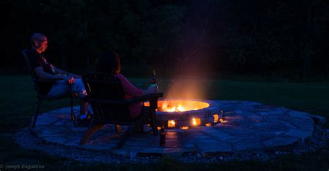 Two People Sitting In Chairs Around A Fire Pit At Night With Bright