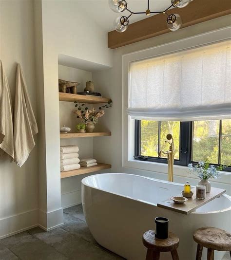 A White Bath Tub Sitting Under A Window Next To A Wooden Shelf Filled