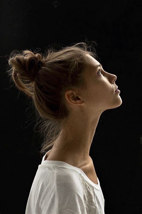 A Woman With Her Hair In A Bun Looking Off To The Side Against A Black