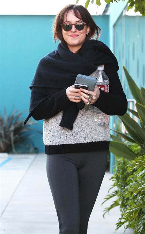 a woman walking down the street while holding a cell phone and wearing leggings