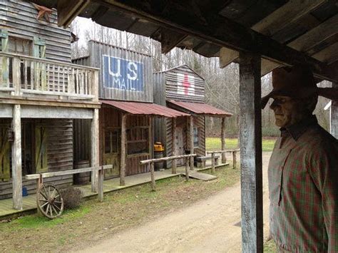 An Old Western Town With Wooden Buildings And A Man Standing In Front