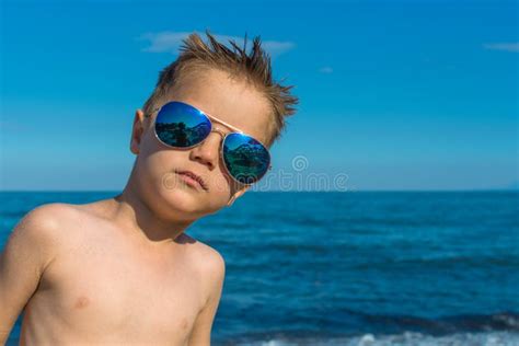 A Beautiful Little Boy Posing On A Beach By The Sea With Sunglasses