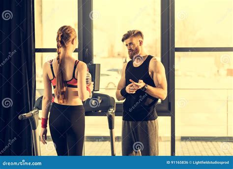 Trainer Instructing Trainee Standing On Treadmill In Gym Stock Photo