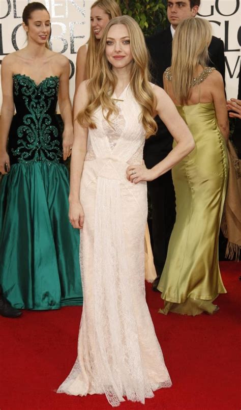 A Woman In A White Dress Standing On A Red Carpet With Other People