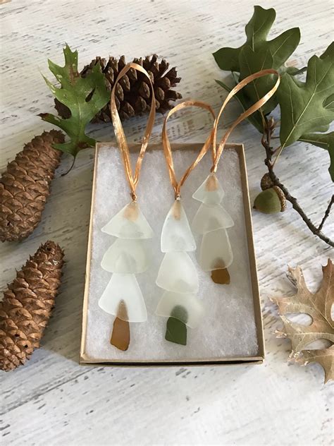 Three White And Green Glass Ornaments In A Box Next To Pine Cones