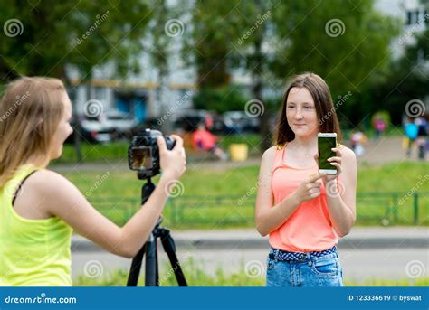 Two Girls Girlfriends In Summer In Park In Nature In Hands Holding A Smartphone Tells About