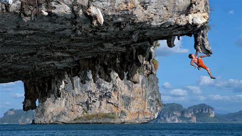 Download Man Climbing Rock Cave Near The Ocean Wallpaper