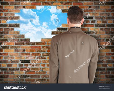 A Business Man Is Facing A Brick Wall With A Hole Of Clouds In It