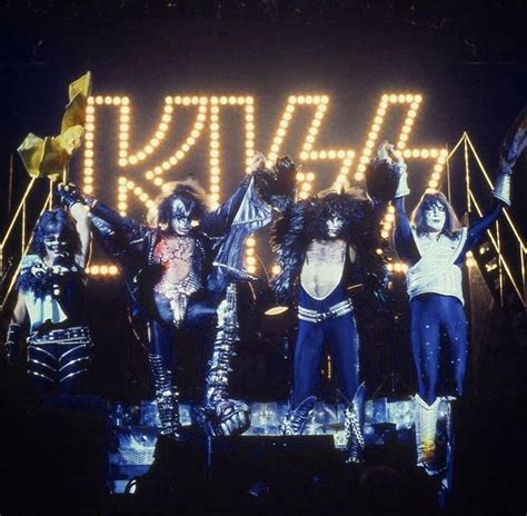 The Kiss Band Performing On Stage With Their Arms In The Air And Lights