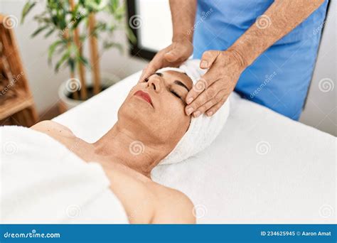 Middle Age Man And Woman Wearing Therapist Uniform Having Facial Massage Session At Beauty