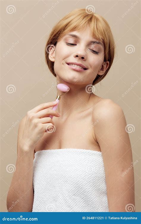 A Joyful Blonde Woman Stands On A Beige Background Wrapped In A Towel