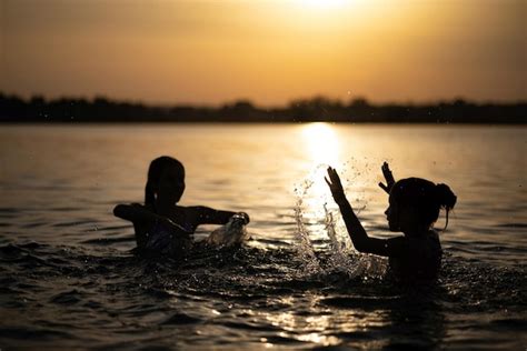 Premium Photo Two Sisters Splashing Water Playing In The Lake At Sunset Background