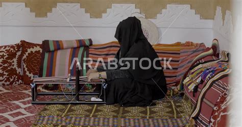 سيدة عربية خليجية سعودية منقبة تقوم بحياكة وغزل الانسجة والقماش، صناعات تقليدية شعبية، حرف يدوية