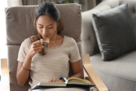 satisfied woman drinking coffee and reading book on armchair at home stock image image of