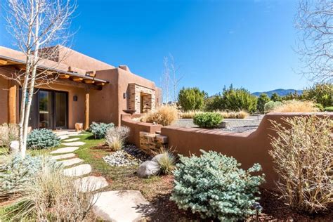 An Adobe Style Home In The Desert Surrounded By Trees And Shrubs With