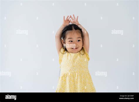 portrait of pleased preschooler and asian girl standing with hands above head isolated on grey