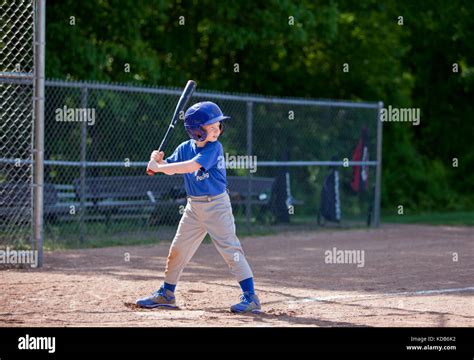 Boy Hitting Ball Whilst Playing Baseball In A Blue Uniform Stock Photo