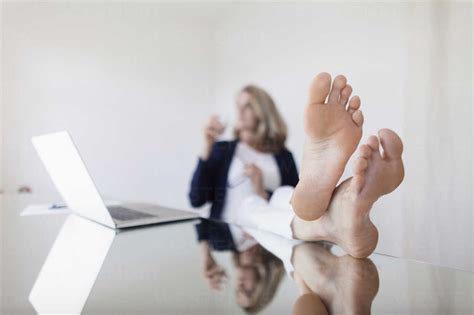 Woman With Legs Crossed At Ankle Resting By Laptop On Table In Office