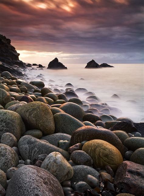 A Rocky Beach Covered In Lots Of Rocks Next To The Ocean Under A Cloudy Sky