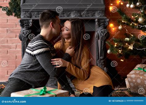 Young Couple In Love Sitting By Fireplace Near Christmas Tree On A Date