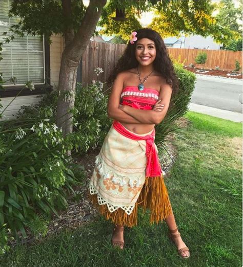 A Woman In A Hula Skirt Standing Next To A Tree With Her Arms Crossed
