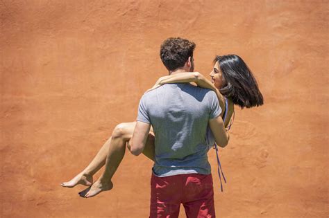 Young Man Carrying Woman While Standing Near Brown Wall At Back Yard
