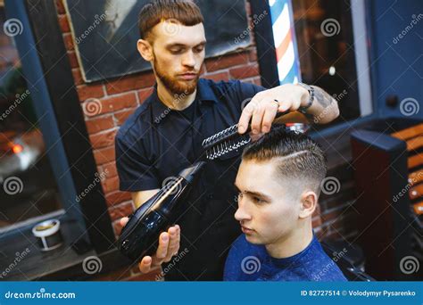Man Getting Groomed By Hairdresser With Hair Dryer At Barbershop Stock