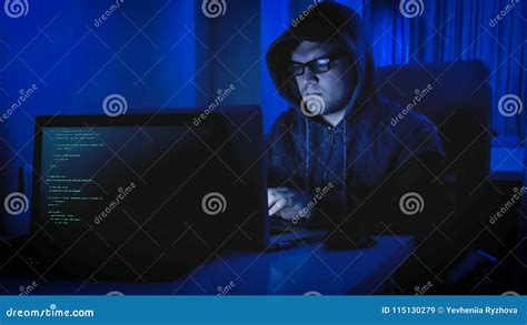 Portrait Of Male Hacker In Hoodie Sitting In Dark Room And Working On