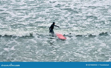 Male Surfer In Black Swimsuit With Red Surfboard In Sea Waves Editorial