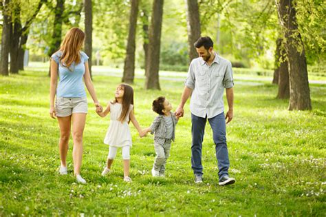 Happy Parents And Little Children Are Holding Hands In Park Stock Photo