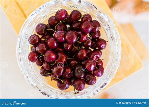 A Glass Bowl Filled With Cherries Of Various Red Shades On A Wooden Platter Stock Photo Image