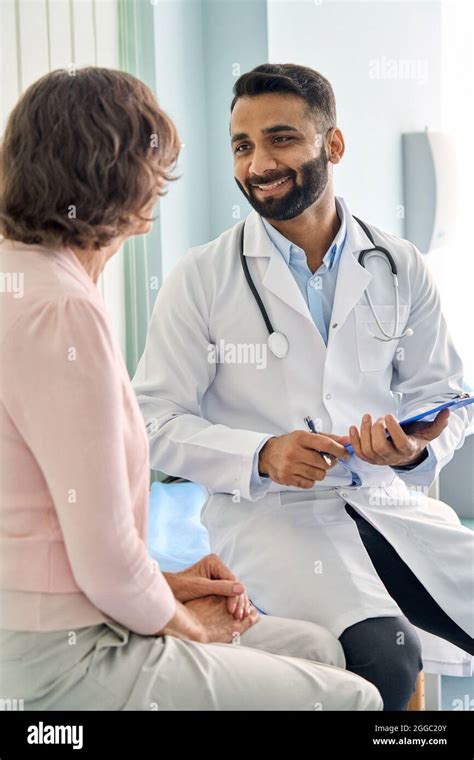 Happy Indian Doctor Consulting Female Older Patient In Hospital