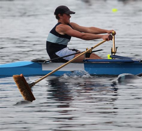 A Man In A Hat Rowing A Blue Boat On The Water With Paddles And Oars