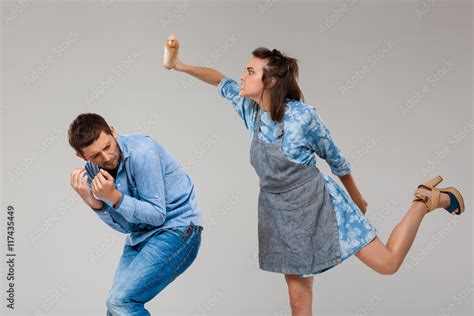 Young Woman Beating Man With Rolling Pin Over Grey Background Stock