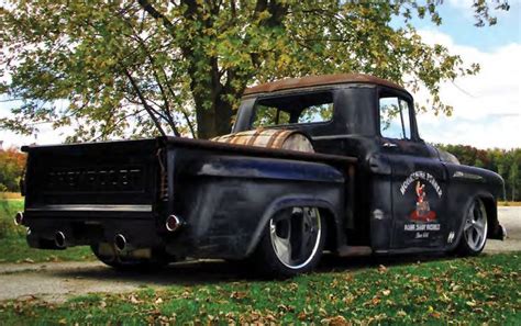 An Old Black Truck Parked On The Side Of A Road In Front Of A Tree