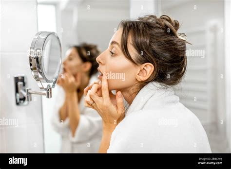 Young Woman In Bathrobe Taking Care Of Her Skin Looking At The Mirror And Worrying About