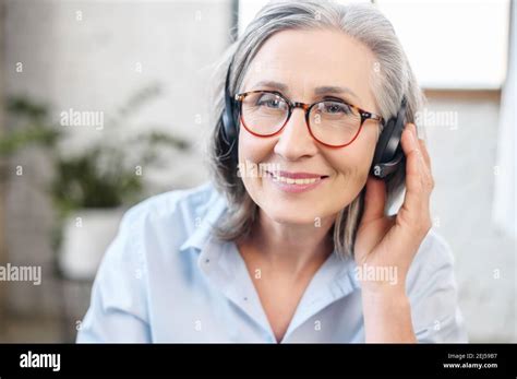 Headshot Portrait Of A Charming Smiling Elegant Senior Lady Wearing Headset Glasses Looking At