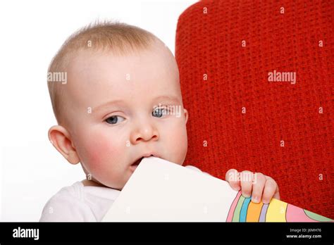 Happy Six Month Old Baby Boy Sitting On A Red Sofa Making Facial