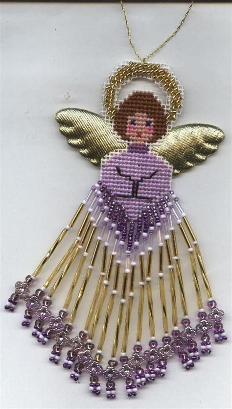 a cross stitch angel ornament with purple beads and gold chains on a ...