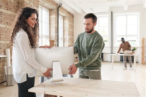 Assisting Colleague To Put Computer On Table In New Office Stock Photo