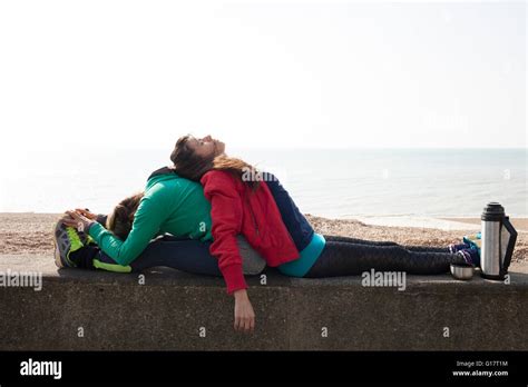 Exhausted Female Runners Leaning Against Each Other On Wall At Brighton
