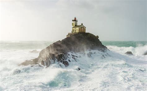 A picturesque lighthouse sits on top of a rock as powerful waves ...