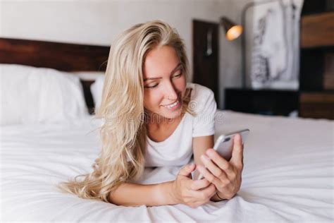 smiling appealing girl lying in bed with phone gorgeous blonde woman chilling in bedroom and