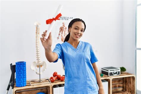 Young African American Woman Wearing Physio Therapist Uniform Holding Diploma At Clinic Stock