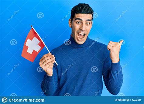 Handsome Hispanic Man Holding Switzerland Flag Pointing Thumb Up To The