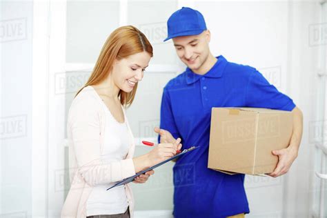 Young Courier Looking At Attractive Young Woman Signing In Delivery
