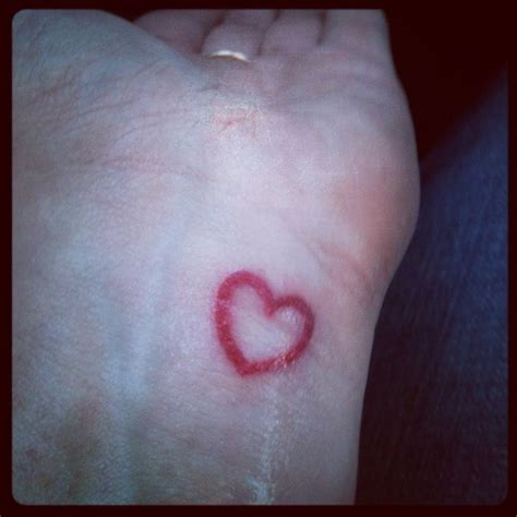 A Small Red Heart Tattoo On Someones Left Foot In The Middle Of Their Arm