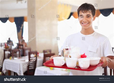Young Smiling Affable Waiter Keeps Tray With Dishes At Restaurant Wide